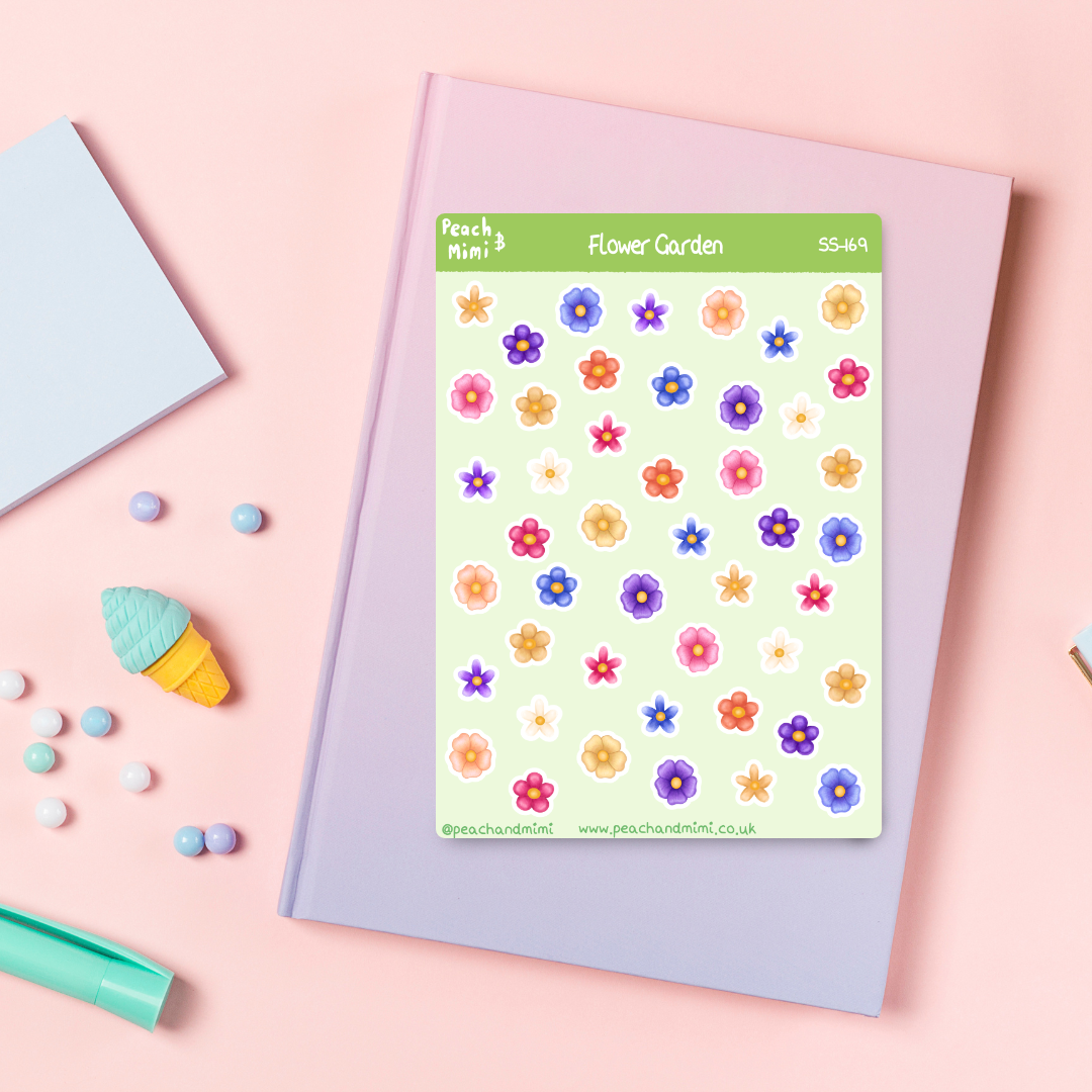 A sticker sheet with various illustrated flowers displayed on a pink background, with a notebook, and other stationery items