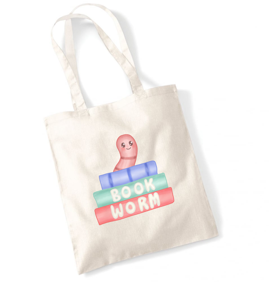 Tote bag with a printed cute illustration of a book worm peeping out over a stack of books that have the words book worm printed on the spines. 