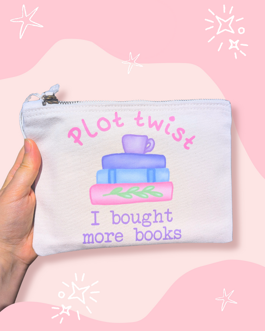 A hand holds a white zippered pouch with a colorful illustration of stacked books and a mug, with the text 'Plot twist I bought more books' on a pink and light pink background with white star doodles.